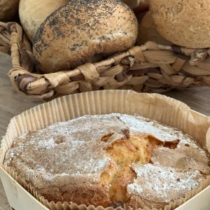 A rustic display of artisan bread and a powdered sugar cake in a woven basket, perfect for bakery themes.