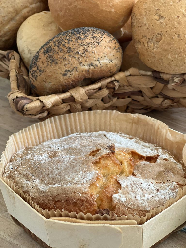 A rustic display of artisan bread and a powdered sugar cake in a woven basket, perfect for bakery themes.